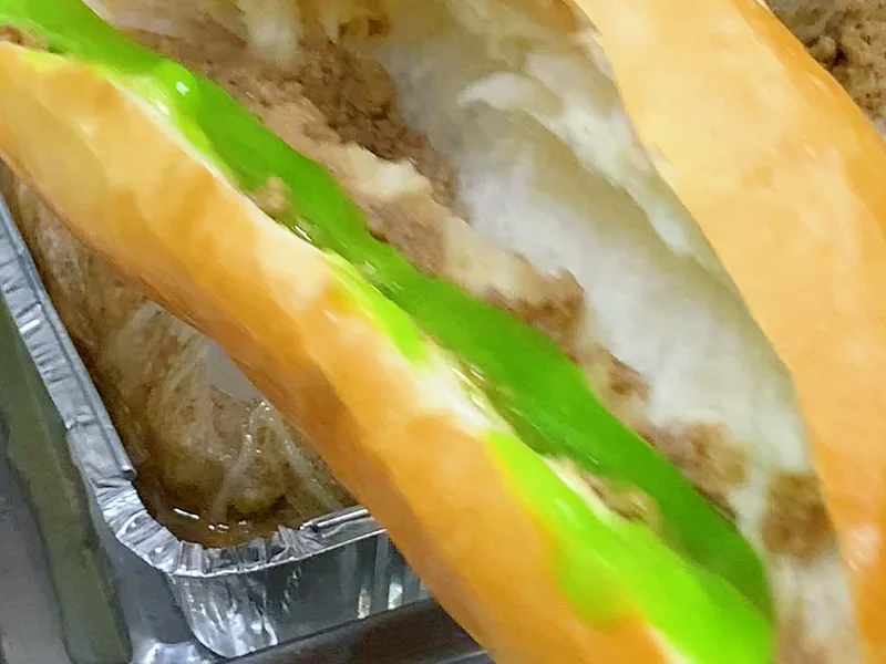 Ổ bánh mì phết sốt bơ cốm xanh dọc theo ruột bánh — khung hình từ video bài học khoá Bánh Mì Kinh Doanh