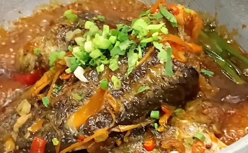 Cá kho tộ trong nồi kim loại viền bạc, nước kho sánh màu cánh gián, rắc hành lá và ớt tươi, món thật của Bếp Cô Linh