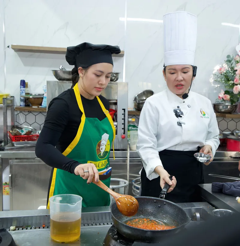 Cô Linh đứng cạnh hướng dẫn học viên xào ớt trên chảo trong lớp học trực tiếp