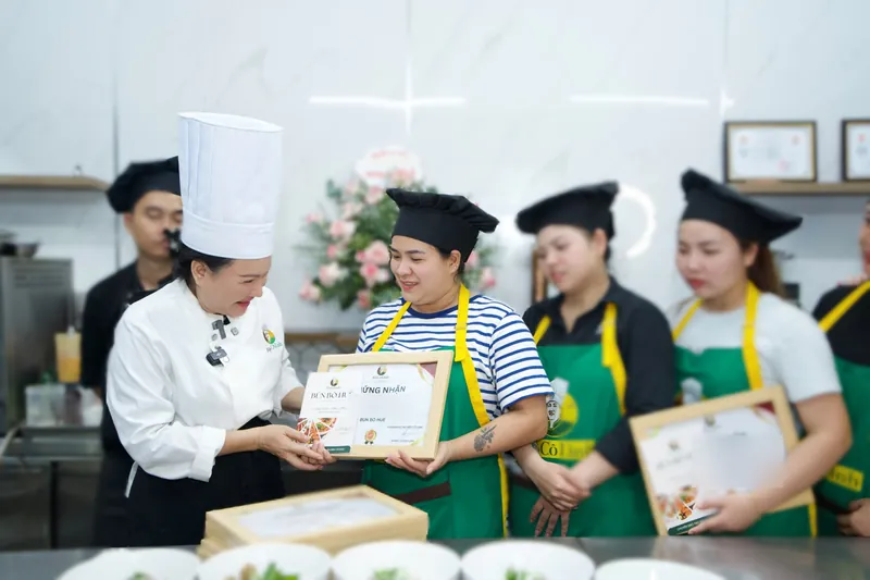 Cô Linh trao chứng nhận hoàn thành khoá Bún Bò Huế cho học viên, các bạn khác đứng cạnh chờ nhận