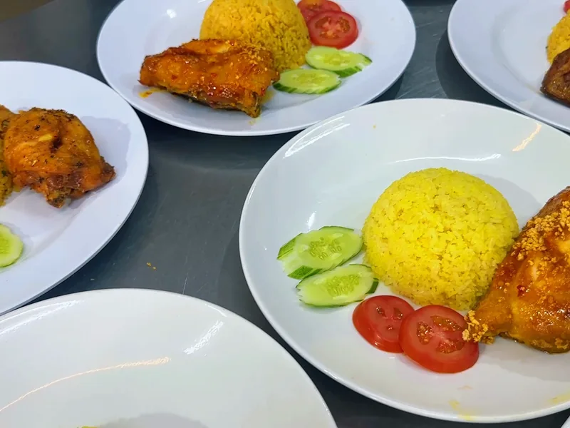 Những đĩa cơm gà xối mỡ bày sẵn với cơm vàng, cà chua và dưa leo — khung hình từ video khoá Cơm Gà Xối Mỡ
