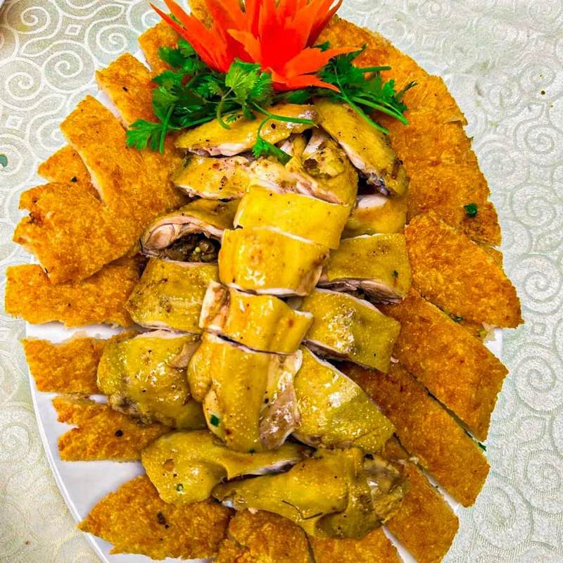 Gà bó xôi trên đĩa bầu dục: phần xôi chiên vàng giòn ôm quanh gà chặt miếng, trang trí hoa cà rốt