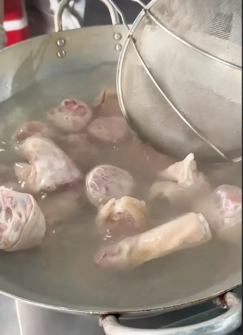 Giò heo đã cạo sạch lông được chần trong nồi nước sôi, vớt bằng vợt lưới tại lớp học Bếp Cô Linh