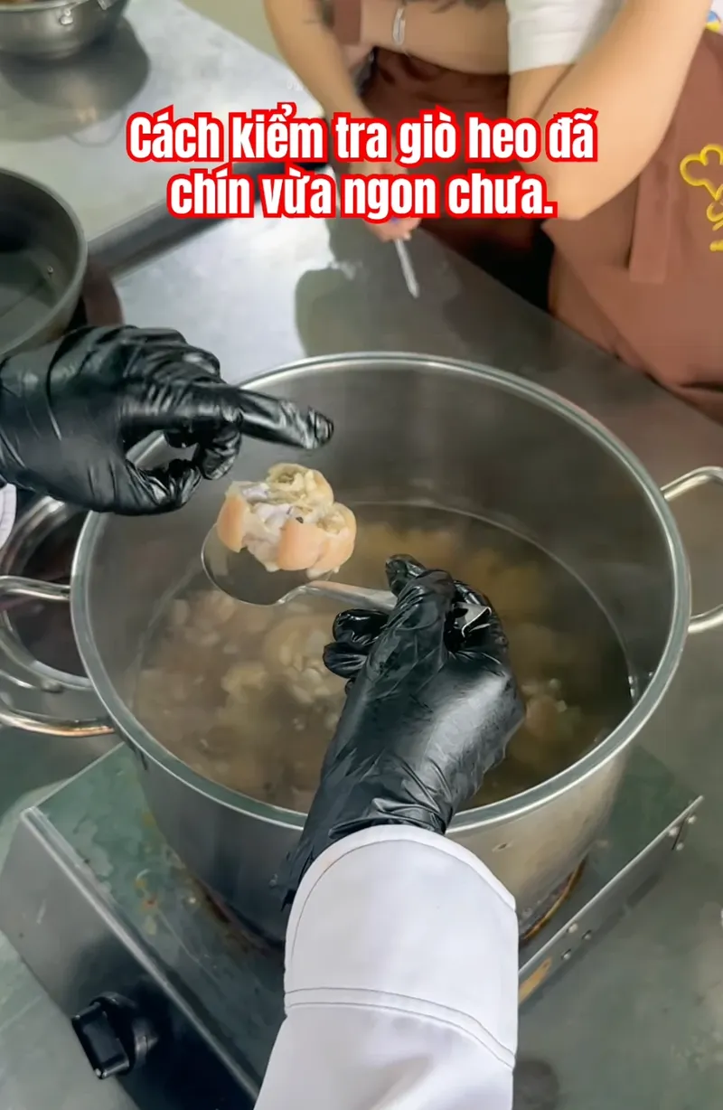 Cô Linh dùng muỗng vớt một miếng giò heo ra kiểm tra độ chín khi luộc tại lớp học Bếp Cô Linh