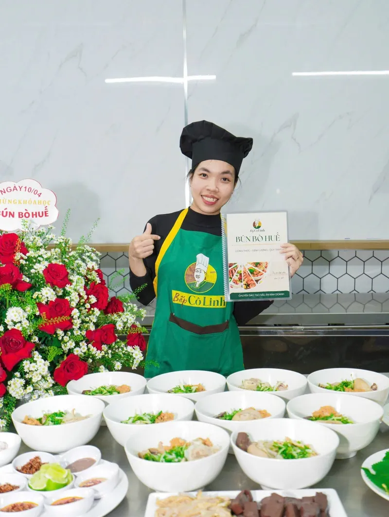 Học viên cầm sổ công thức Bún Bò Huế, phía trước là các tô bún thành phẩm và chén gia vị