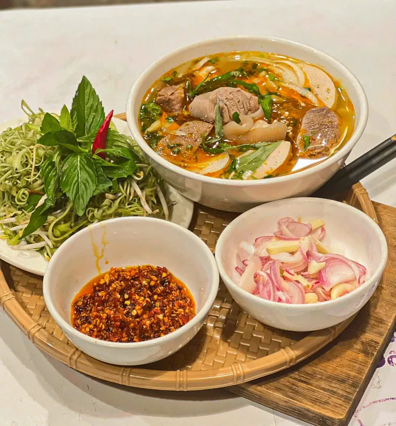 Thành quả của học viên Bếp Cô Linh gửi cho cô: tô bún bò Huế ăn kèm đĩa rau sống, chén sa tế và hành tây ngâm