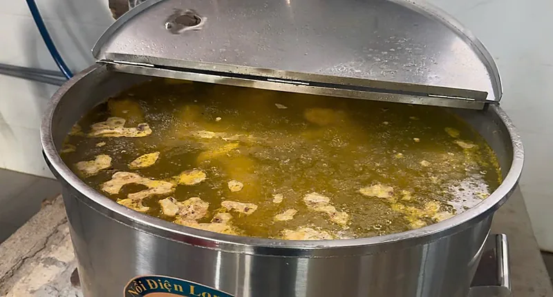 Nồi điện inox đang hầm xương nấu nước dùng phở bò, nước màu vàng, nắp mở một nửa