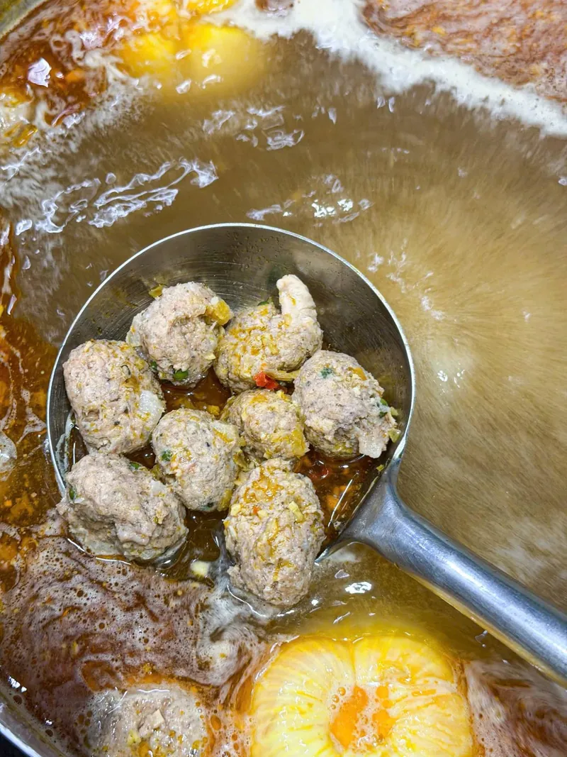 Nước lèo bún bò Huế trong màu vàng nâu nhạt trong nồi lớn, chả viên đang nổi trên mặt