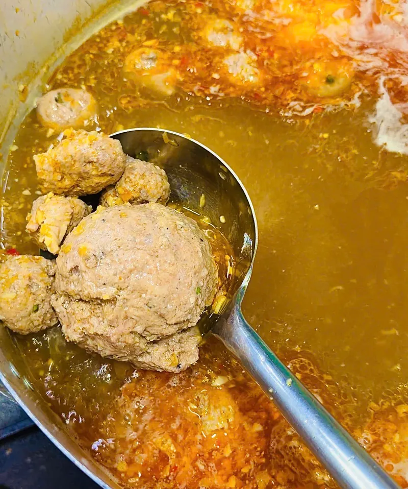 Nồi nước lèo bún bò Huế trong màu hổ phách, đang nấu cùng chả viên