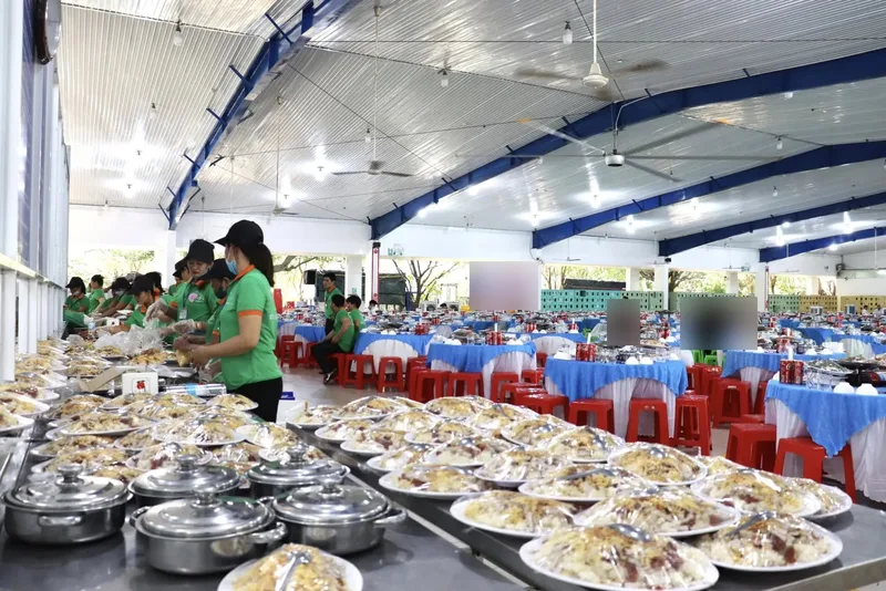 Dãy đĩa món đã xếp sẵn và bọc màng, đội bếp áo xanh lá đang xếp đĩa trước giờ khách vào sảnh tiệc 350 bàn