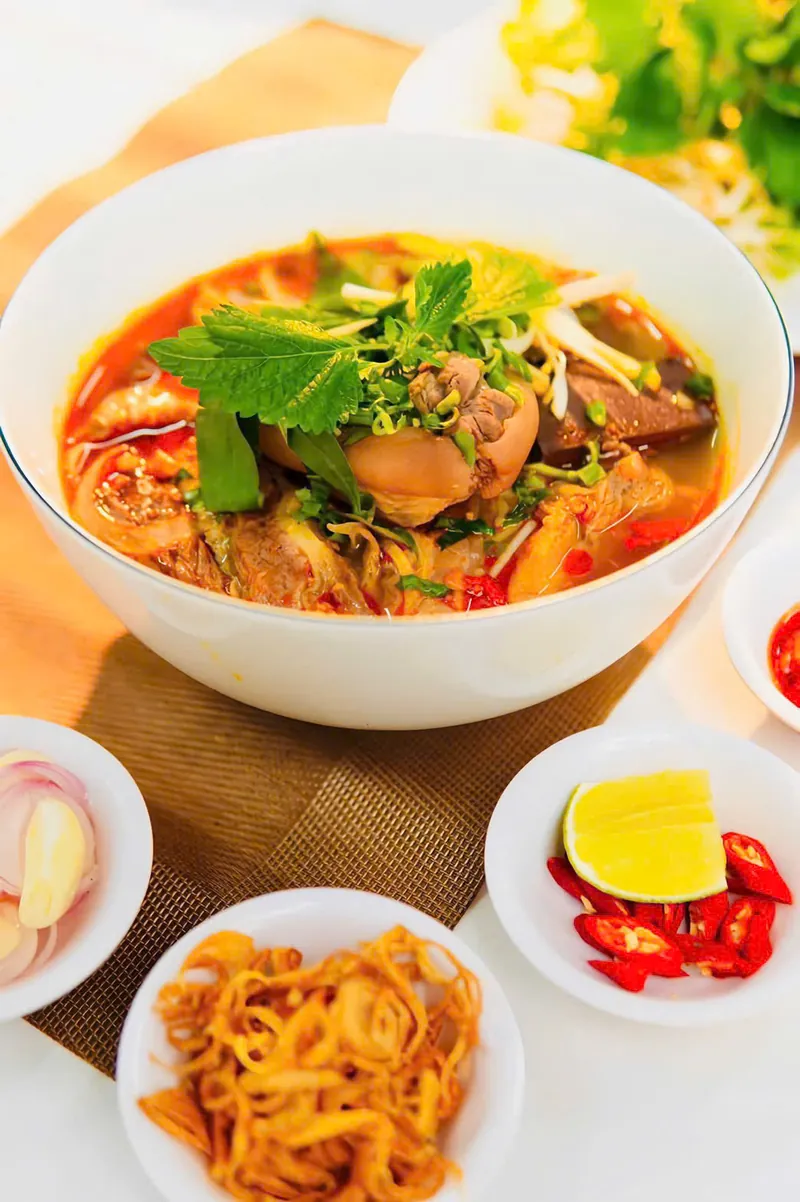 Tô bún bò Huế nước lèo cam đỏ, ăn kèm rau sống, hành tây, ớt và chanh