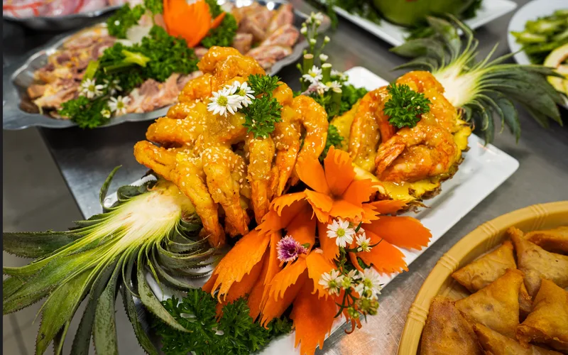Tôm sốt bày trên hai nửa trái thơm, trang trí hoa cà rốt tỉa và rau mùi tây, bên cạnh mâm tiệc